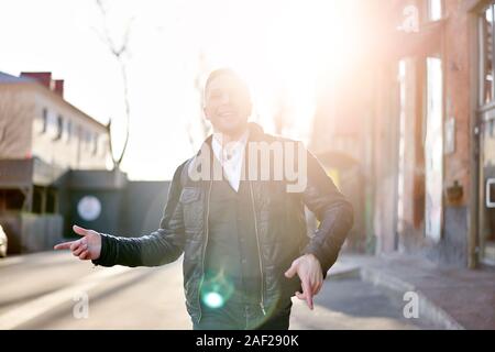 Junge brunet auf Spaziergang in der Stadt gegen den Hintergrund der Gebäude am Tag. Sonnenlicht Wirkung Stockfoto