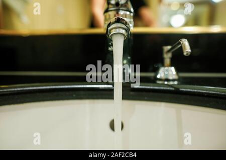 Flache Tiefenschärfe (selektive Fokus) Bild mit laufendem Wasser aus einem Hahn und einem Seifenspender in ein Hotel Bad. Stockfoto