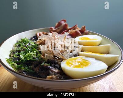 Ramen: Asiatische Nudelsuppe mit Speck, Eier, Pilze, Gemüse, Algen und katsuobushi in eine Schüssel geben. Holz Hintergrund. Stockfoto