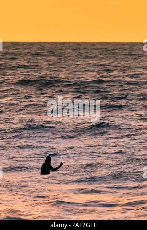 Ein Surfer im Meer wartet auf eine Welle, wie die Sonne in Newquay in Cornwall. Stockfoto