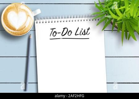 Blick von oben auf die Spiralbindung und Notebook mit Aufgabenliste auf weissem Holztisch mit Topfpflanzen und Tasse Kaffee Stockfoto