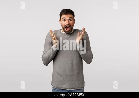 Beeindruckt und begeistert Menschen erhalten Sie tolle Nachrichten. Sprachlos ekstatisch gut aussehender bärtiger Kerl in graue Strickjacke, er gewann, umklammern die Hände kann nicht glauben Stockfoto