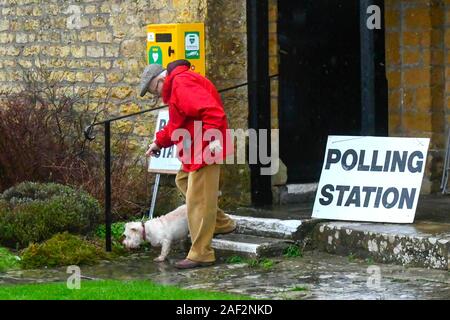 Walditch, Dorset, Großbritannien. 12. Dezember 2019. Ein Mann, der eine wasserdichte Jacke hinterlässt mit seinem Hund im Regen nach der Abstimmung im Wahllokal an Walditch in Dorset auf einem nassen allgemeinen Wahltag. Foto: Graham Jagd-/Alamy leben Nachrichten Stockfoto