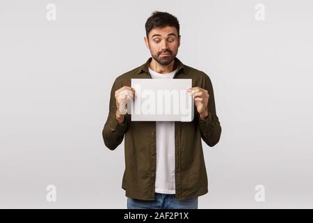 Verwirrt und beschämt cute unentschlossen kaukasischen Mann mit Bart, am leeren Blatt Papier mit Verwirrten, zögernd und unsicher Ausdruck suchen, haben Stockfoto