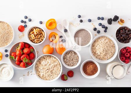 Abwechslungsreiche Auswahl von unverarbeitetem Getreide, Früchte und Nüsse zum Frühstück. Haferflocken Flocken und Stahl schneiden, Gerste, Nussbaum, Chia, Aprikose, Erdbeere. Gesunde Zutaten Stockfoto