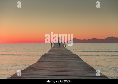 Frau, die auf hölzernen Pier. Sunrise Meer Landschaft im Hintergrund Stockfoto