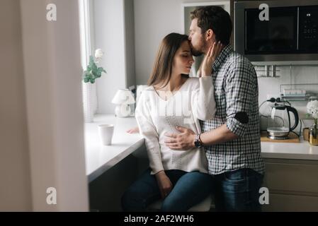 Kerl küsst seine Freundin auf der Stirn in der Küche durch die winndow. Stockfoto