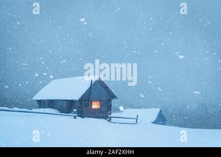 Fantastische Winterlandschaft mit Holzhaus im Schneesturm in Snowy Mountains. Weihnachten und Winter Ferien Konzept Stockfoto