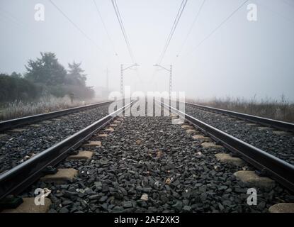 Schienen und Oberleitung Beiträge verschwinden in dichtem Nebel im Land. Zug Konzept Stockfoto