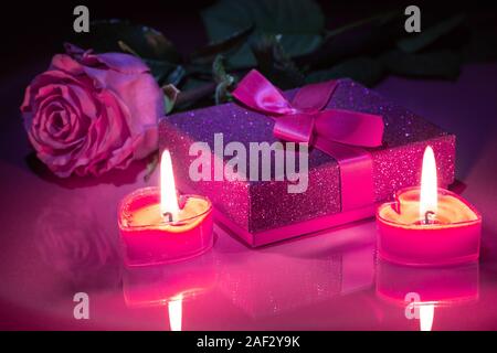 Dunkle Szene von Valentine Geschenk Box mit rosa Rose und brennende Kerzen auf eine reflektierende Tischplatte Stockfoto