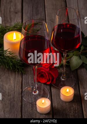 Nahaufnahme von zwei Gläser Wein mit roten Rosen und brennende Kerzen auf einem rustikalen Holztisch Stockfoto