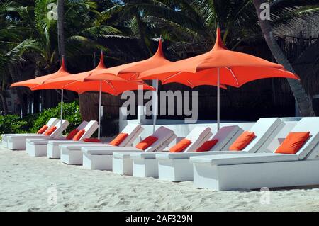 White Lounge Sessel mit Kissen Orange und Orange Regenschirme alle bis in den Sand gezeichnet. Stockfoto