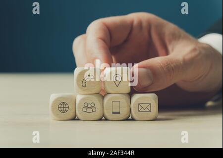 Hand eines Geschäftsmannes stapeln Holz- Würfel mit Kontakt und Informationen Symbole auf Sie in einem konzeptionellen Bild. Stockfoto