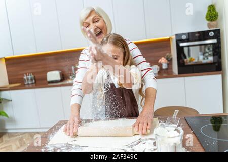 Junge weibliche Bäcker Mehl über den Teig streuen Stockfoto