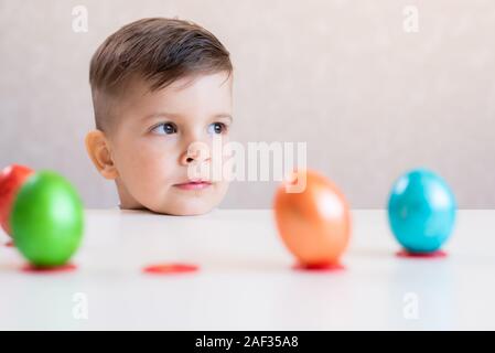 Ein wenig beautiful Boy legte seinen Kopf auf einem weißen Tisch, auf dem in einer Reihe stehen bunte Ostereier auf weißem Hintergrund. Stockfoto