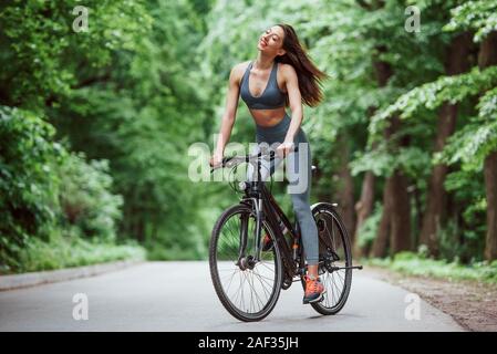 Easy Wind. Weibliche Radfahrer mit dem Rad auf Asphalt Straße in den Wald bei Tag Stockfoto