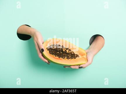 Weibliche Hände halten frischer Papaya durch ein Loch auf Neon mint Hintergrund. Stockfoto