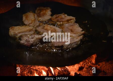 Die koteletts Pan im Feuer gebraten. Pan ist auch das Kochen Fleisch. Schwein Stücke von Fleisch sind auf ein Lagerfeuer auf einer Disc aus einer Egge gekocht. Brocken Fleisch gebraten Stockfoto