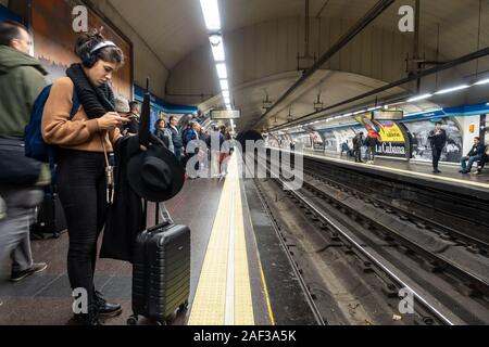 Eine junge Frau mit einem Wheelie Fall mit Ihrem Mobiltelefon, während sie darauf warteten, dass ein Zug am Tribunal Madrider U-Bahn Station. Stockfoto