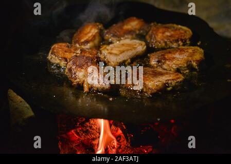 Die koteletts Pan im Feuer gebraten. Pan ist auch das Kochen Fleisch. Schwein Stücke von Fleisch sind auf ein Lagerfeuer auf einer Disc aus einer Egge gekocht. Brocken Fleisch gebraten Stockfoto