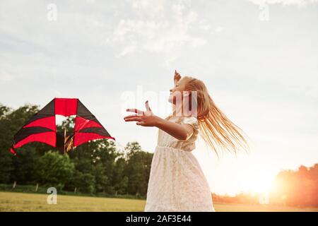 Fast klaren Himmel. Glückliches Mädchen in weißen Kleidern viel Spaß mit Kite im Feld. Schöne Natur Stockfoto