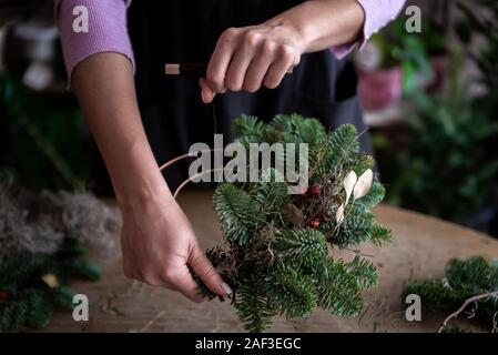 Frau, die Weihnachten Kranz von Fichte, Schritt für Schritt. Konzept der Floristen Arbeiten vor den Weihnachtsferien. Stockfoto