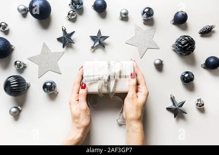 Weihnachten Zusammensetzung der klassischen blauen Kugeln und Geschenkbox in womans Hand auf Grau. Ansicht von oben. Weihnachten. Urlaub Grußkarte. Trendfarbe des Jahres 2020. Stockfoto