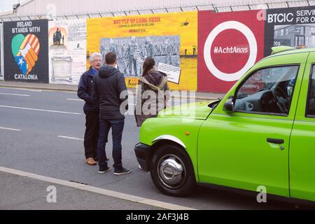 Grüne traditionellen cab auf einer Tour von Belfast, mit Fahrer, Geschichte der Mühen zu zwei Touristen vor über Frieden Art Wall Stockfoto
