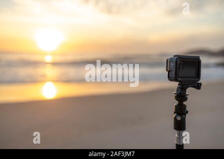 GoPro Hero 7 auf einem Stativ auf einem Strand in Rio taping und den Sonnenaufgang mit der Sonne im Meer Wasser widerspiegeln Stockfoto