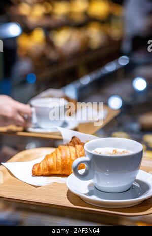 Kaffee und Croissant serviert in einem Fach auf der Theke in einem verschwommenen Konditorei Hintergrund Stockfoto