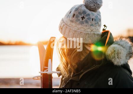 Frau, die mit ihren Skiern bei Sonnenuntergang im Winter Stockfoto