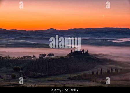 Typische hügelige Toskanische Landschaft im Val d'Orcia, der Bauernhof Podere Belvedere auf einem kleinen Hügel und Nebel in den Tälern, bei Sonnenaufgang Stockfoto