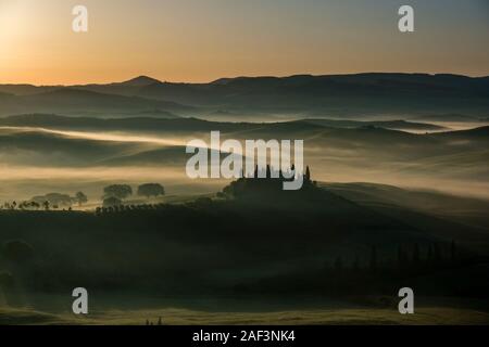 Typische hügelige Toskanische Landschaft im Val d'Orcia, der Bauernhof Podere Belvedere auf einem kleinen Hügel und Nebel in den Tälern, bei Sonnenaufgang Stockfoto