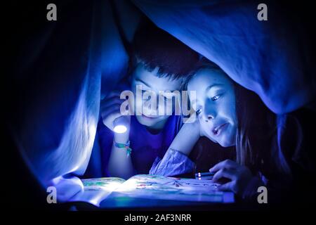 Kinder lesen eine Geschichte mit Taschenlampen unter einer Decke Stockfoto