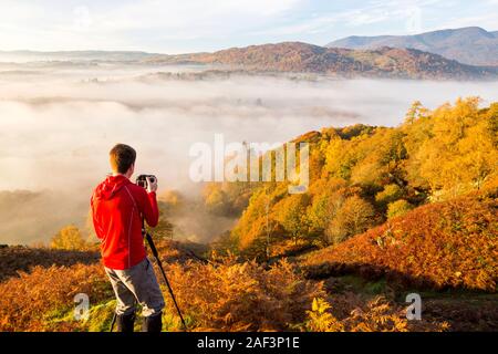 Tal-Nebel über Lake Windermere von Todd Crag im Lake District, Großbritannien bei Sonnenaufgang mit einem Fotografen im Vordergrund. Stockfoto