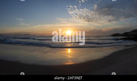 Super Wide Panorama der Wellen am Strand des Arpoador Teufel in Rio de Janeiro, Brasilien, bei Sonnenaufgang mit der Sonne im Wasser widerspiegelt Stockfoto