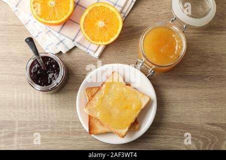 Toast auf Platte, Marmelade, Handtuch und orange auf hölzernen Hintergrund, Ansicht von oben Stockfoto