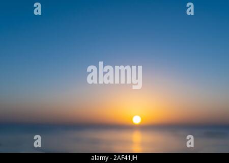 Defokussierten Sonnenuntergang unter strahlend blauem Himmel Hintergrund Bild über das ruhige Meer. Stockfoto