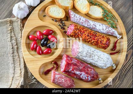 Sortiment von Salami mit Häppchen auf hölzernen Hintergrund: Ansicht von oben Stockfoto