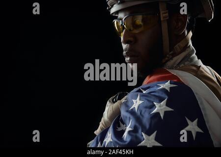 Blick von der Schulter der afrikanischen Soldaten mit National Flagge posing mutig. Ernst ranker tragen Uniform, Helm und Brille. Zurück isoliert Hintergrund. Stockfoto