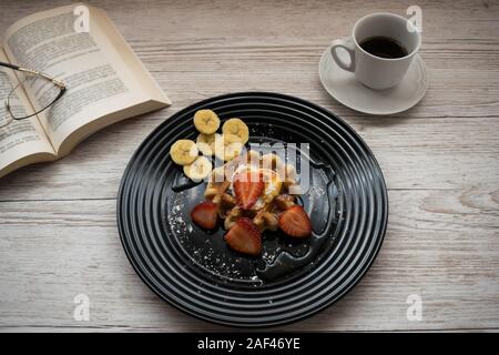 Leckere Waffeln mit Früchten auf einem Tisch mit einem Kaffee und einem Buch Stockfoto