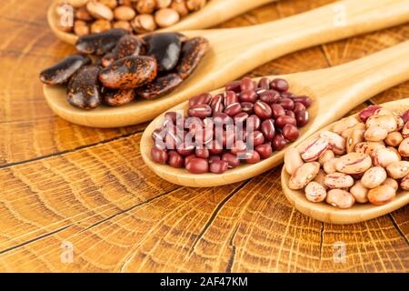 Verschiedene Bohnen in der Kochlöffel auf den braunen Hintergrund. Stockfoto