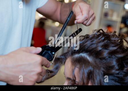 Friseur Haar über richten. blond Tun der Lockenstab im Schönheitssalon. Professionelle Friseur. Mit Schließen der Stylist hand Stockfoto