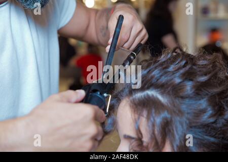 Friseur Haar über richten. blond Tun der Lockenstab im Schönheitssalon. Professionelle Friseur. Mit Schließen der Stylist hand Stockfoto