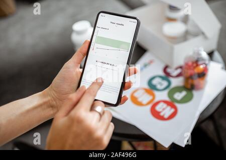 Frau überprüfen das Ergebnis der medizinischen Tests auf einem Smartphone, close-up mit Nahrungsergänzung auf dem Hintergrund. Konzept der individuellen Auswahl von online Nahrungsergänzungsmittel Stockfoto