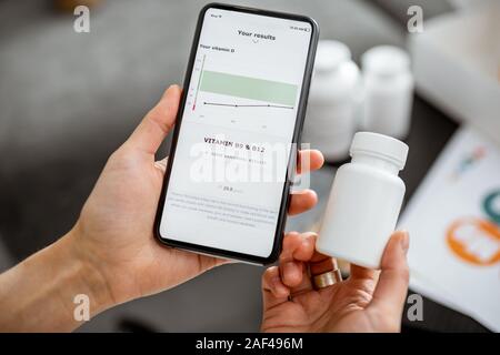 Frau überprüfen das Ergebnis der medizinischen Tests auf einem Smartphone, close-up mit Nahrungsergänzung auf dem Hintergrund. Konzept der individuellen Auswahl von online Nahrungsergänzungsmittel Stockfoto