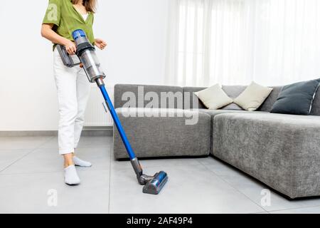 Frau Reinigung Boden mit Cordless Vacuum Cleaner in der modernen weißen Wohnzimmer. Konzept der einfache Reinigung mit einem drahtlosen Staubsauger Stockfoto