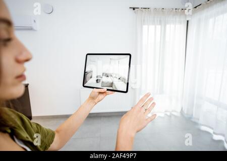 Junge Frau, neue Möbel auf einem digitalen Tablet in den leeren Innenraum, schauen, wie es aussieht, bevor Sie kaufen. Konzept der Augmented Reality in Design und Retail Business Stockfoto