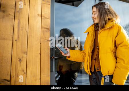 Frau Verriegelung smartlock Auf der Eingangstür mit einem Smart Phone. Konzept der Verwendung von Smart elektronische Schlösser mit Keyless Access Stockfoto