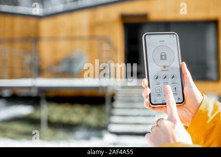 Halten Sie das Telefon mit gestartet alarm App auf das Haus Hintergrund im Freien. Konzept der Steuerung und Verwaltung Startseite sicherheit von einem mobilen Gerät Stockfoto